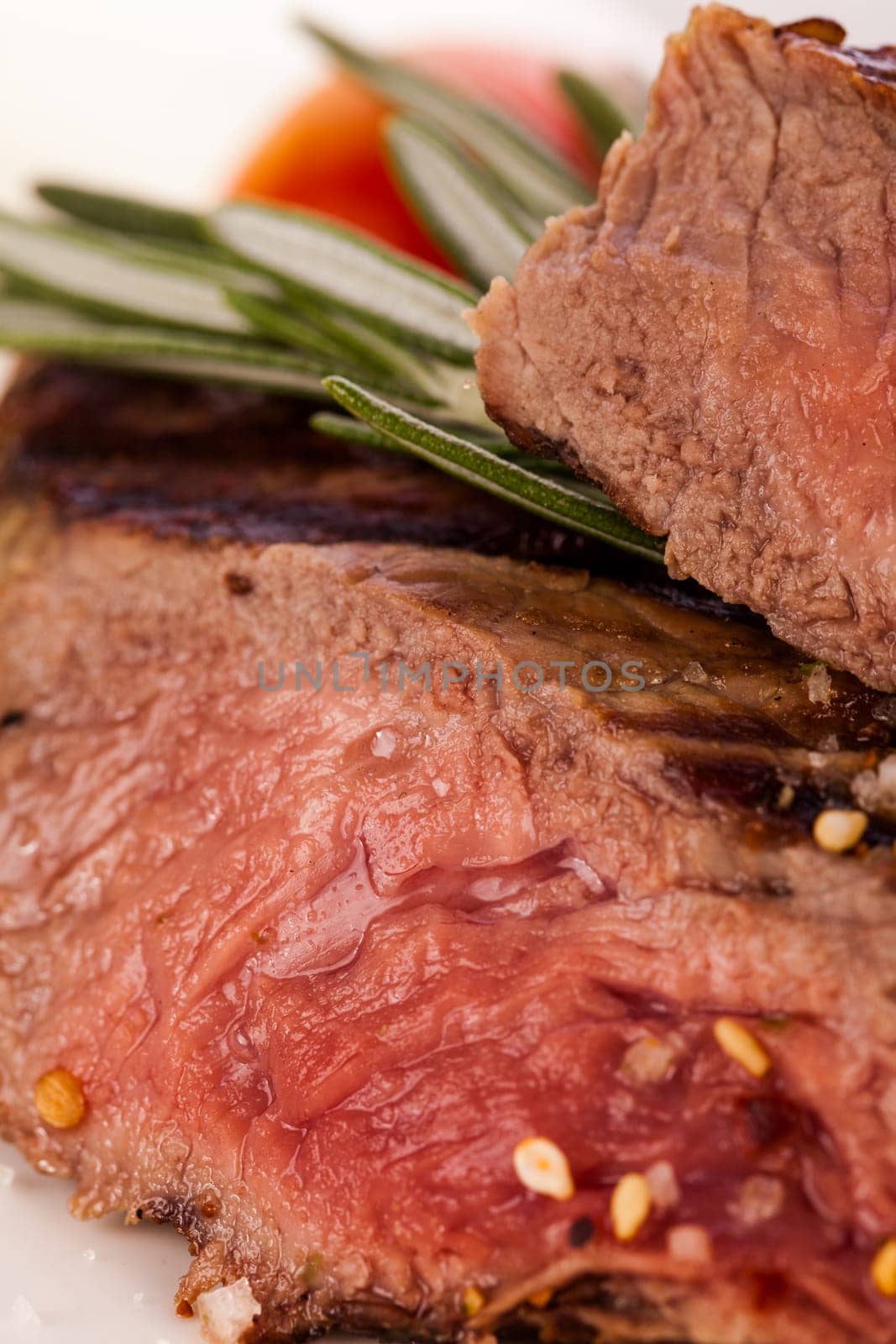 Medium fried beef steak fillet with pepper and rosemary sliced on a plate insulated against white background