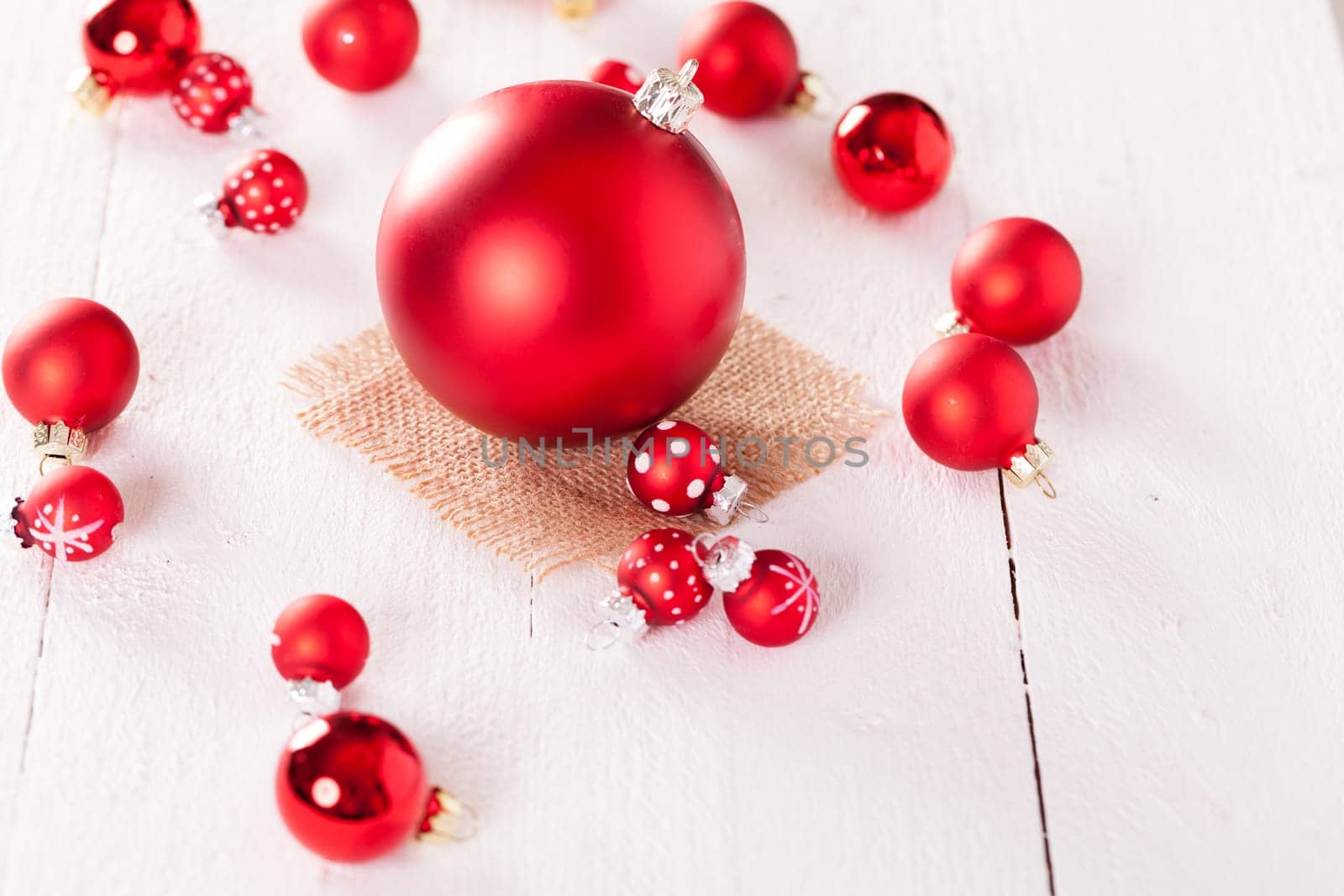large and small red Christmas tree balls on a wooden board with a jutesack as a close-up