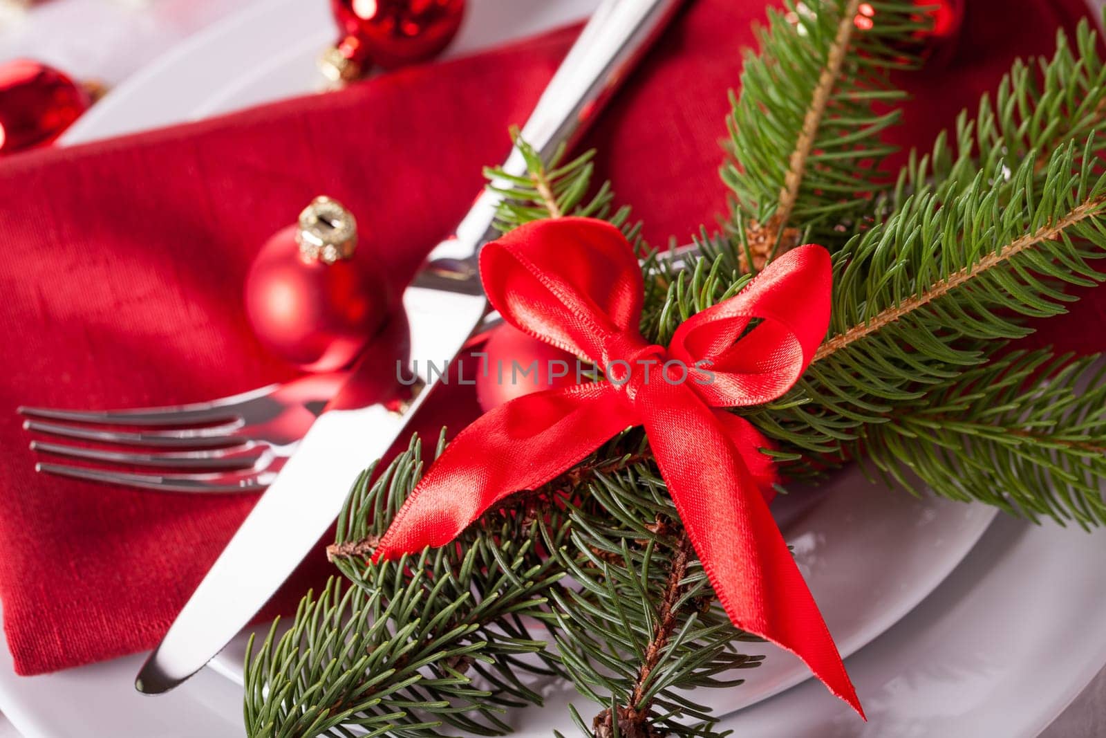 Red napkin with Christmas glass balls and cutlery with a green fir branch and red bow close-up