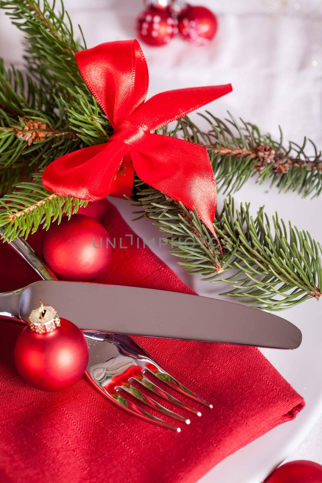 Red napkin with Christmas glass balls and cutlery with a green fir branch and red bow close-up