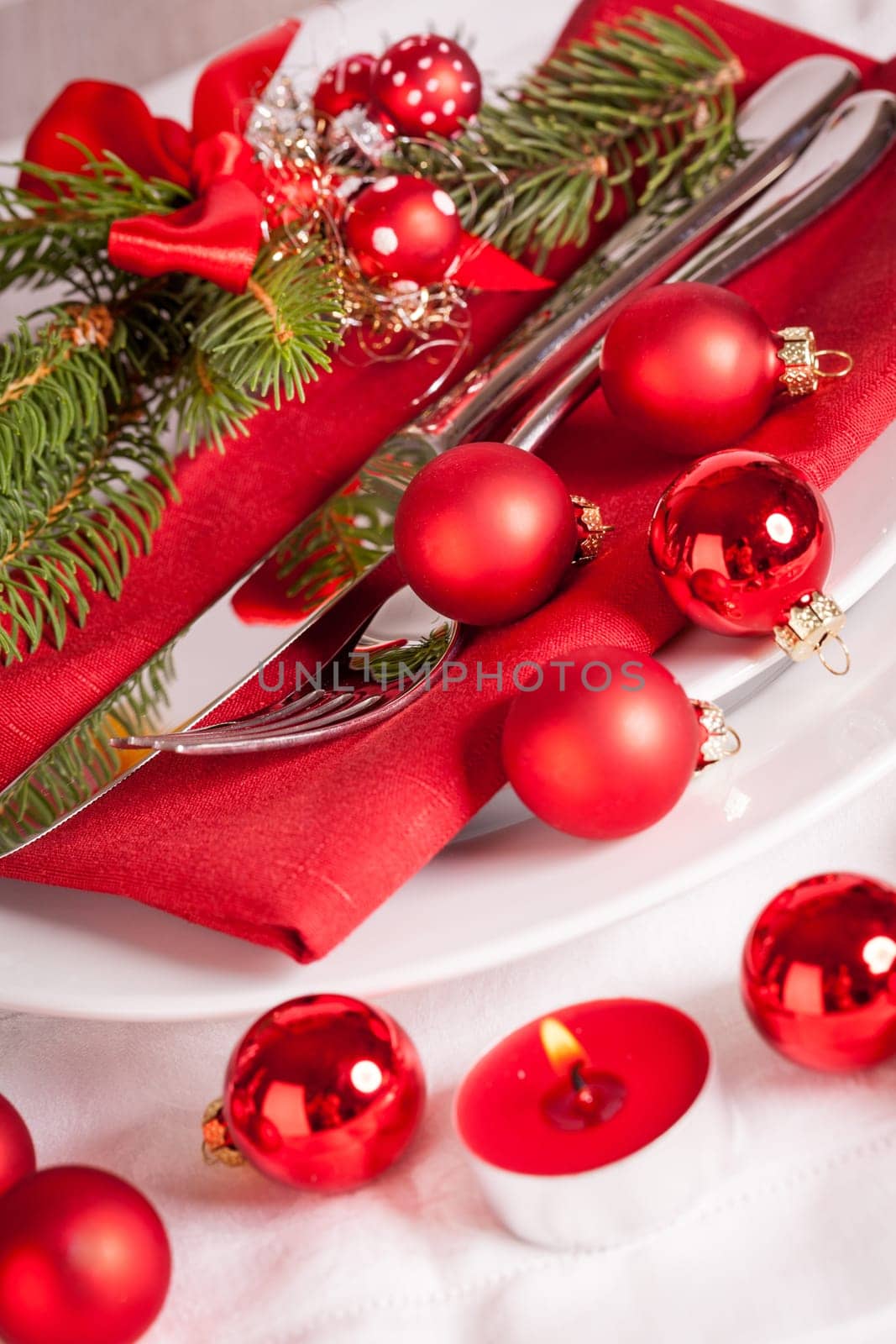 Red napkin with Christmas glass balls and cutlery with a green fir branch and red bow close-up
