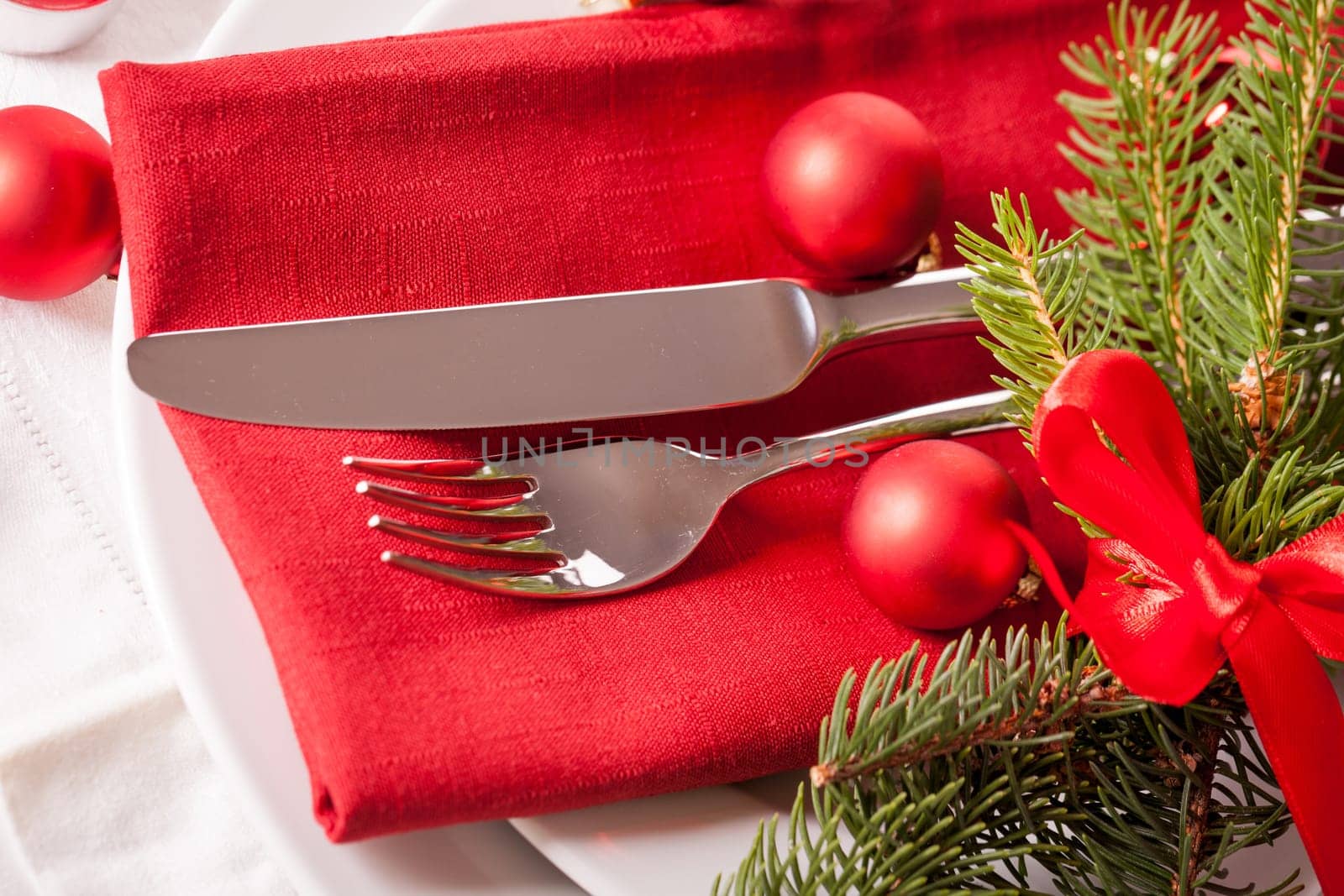 Red napkin with Christmas glass balls and cutlery with a green fir branch and red bow close-up