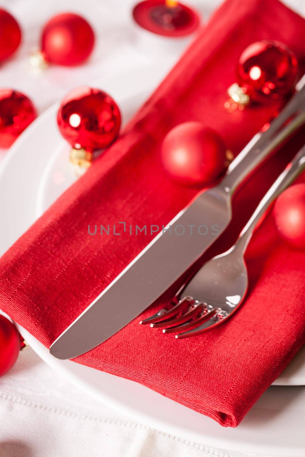 Red napkin with Christmas glass balls and cutlery with a green fir branch and red bow close-up