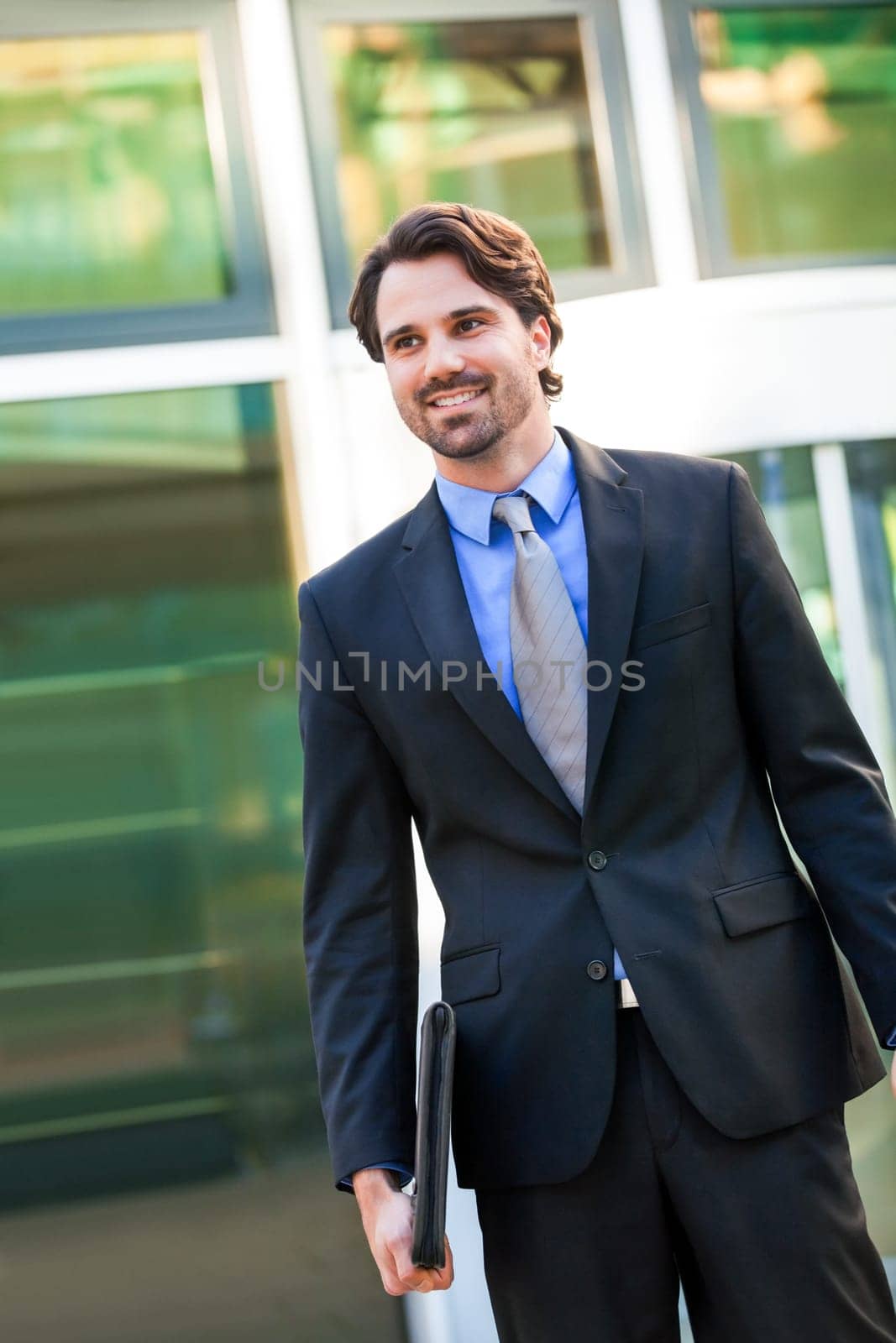 Young trendy businessman in front of a business building successfully with beard and dark hair