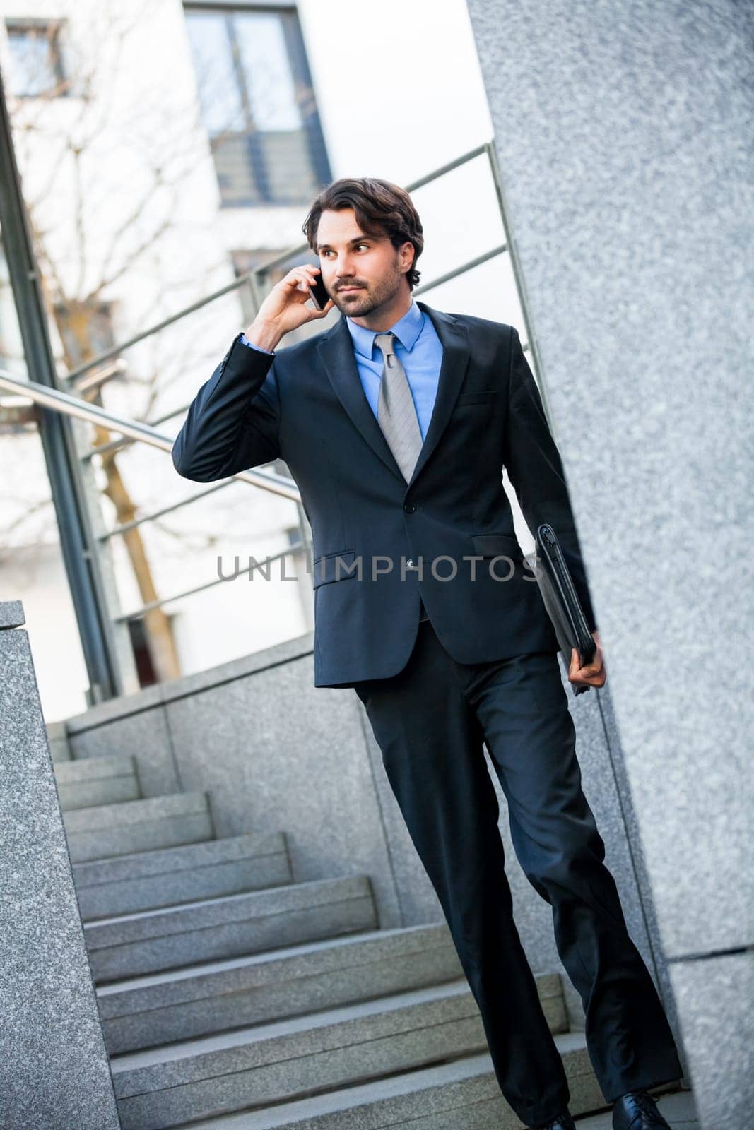 Young trendy successful businessman with mobile phone smartphone cheerful lyrane in front of an outdoor business building