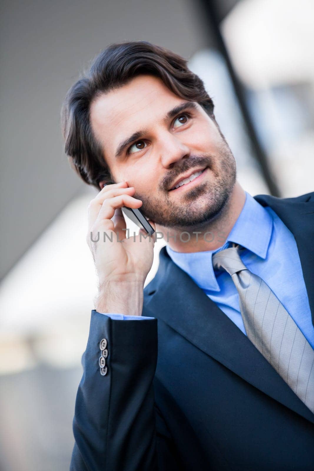 Young trendy successful businessman with mobile phone smartphone cheerful lyrane in front of an outdoor business building