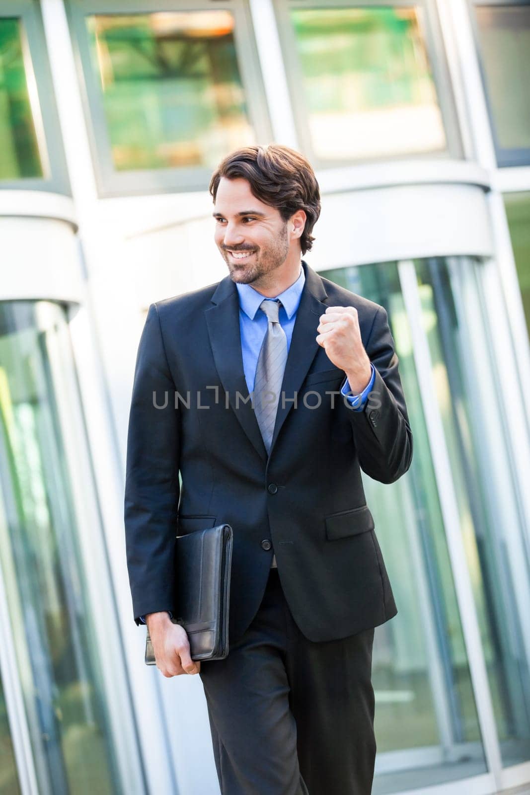 Attractive young businessman cheering in front of a business building in the summer
