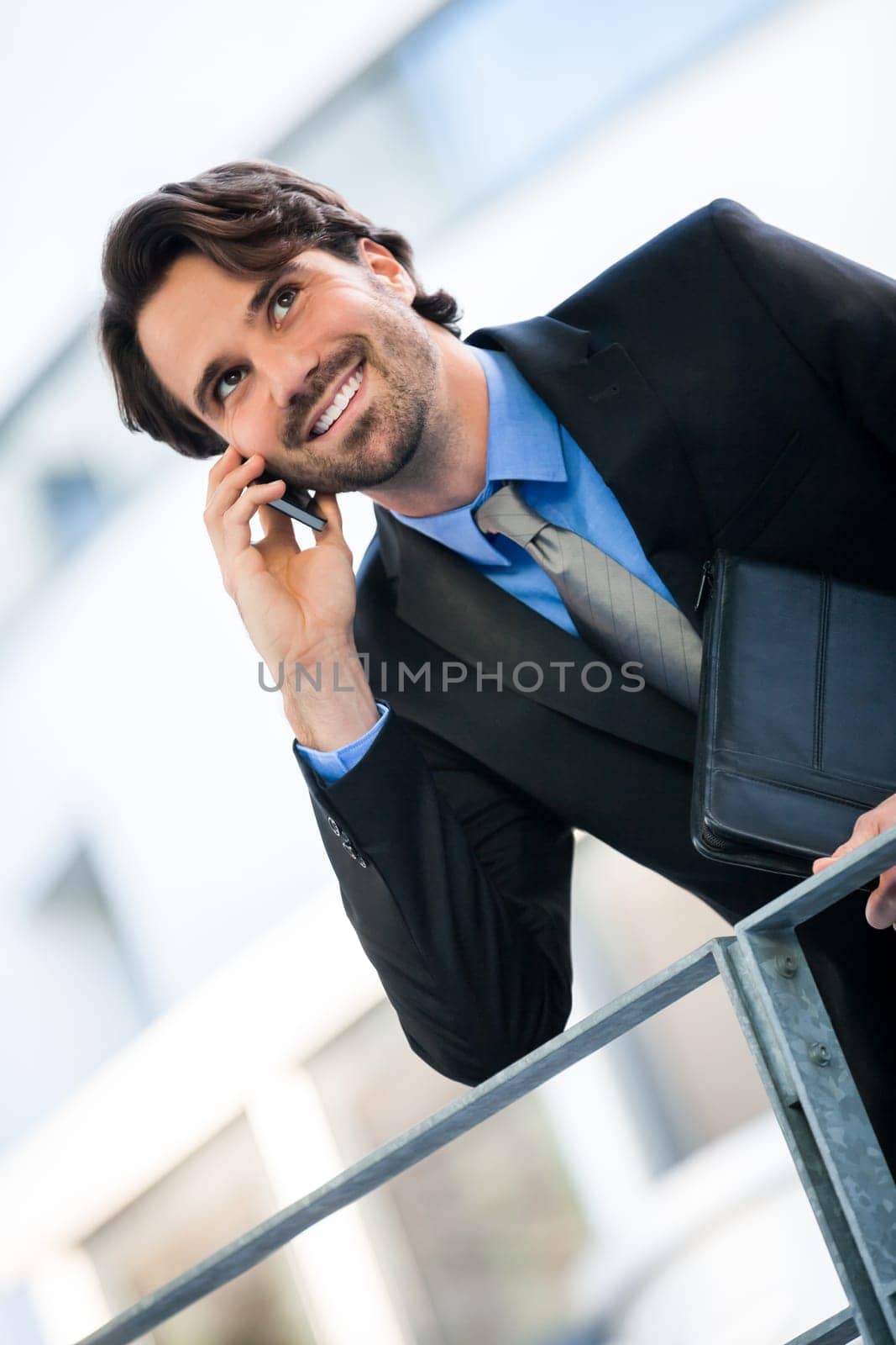 Young trendy successful businessman with mobile phone smartphone cheerful lyrane in front of an outdoor business building
