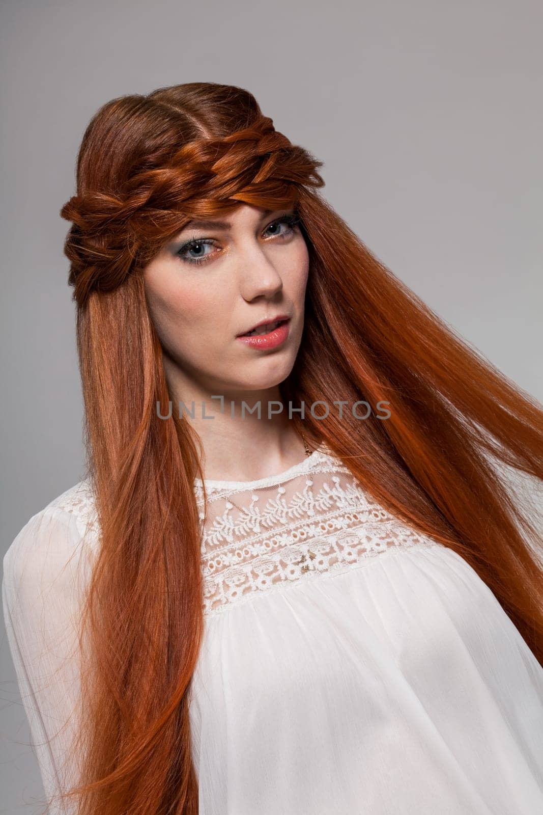 Young attractive female girl with long red hair in portrait against grey background
