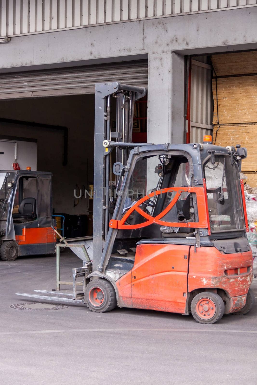 Small orange forklift in front of a warehouse with freight traffic and goods in the background