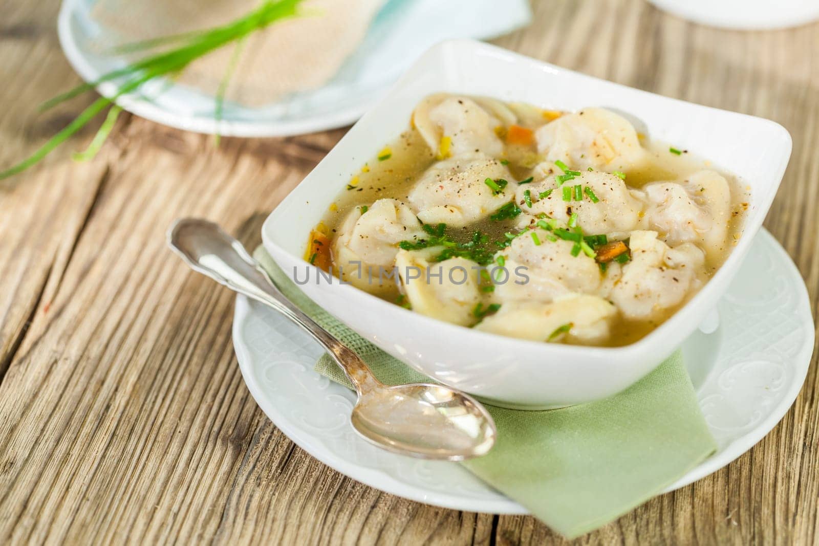 Bowl with Russian Pelmeni Italian tortellini with broth and parsley close-up on a wooden table