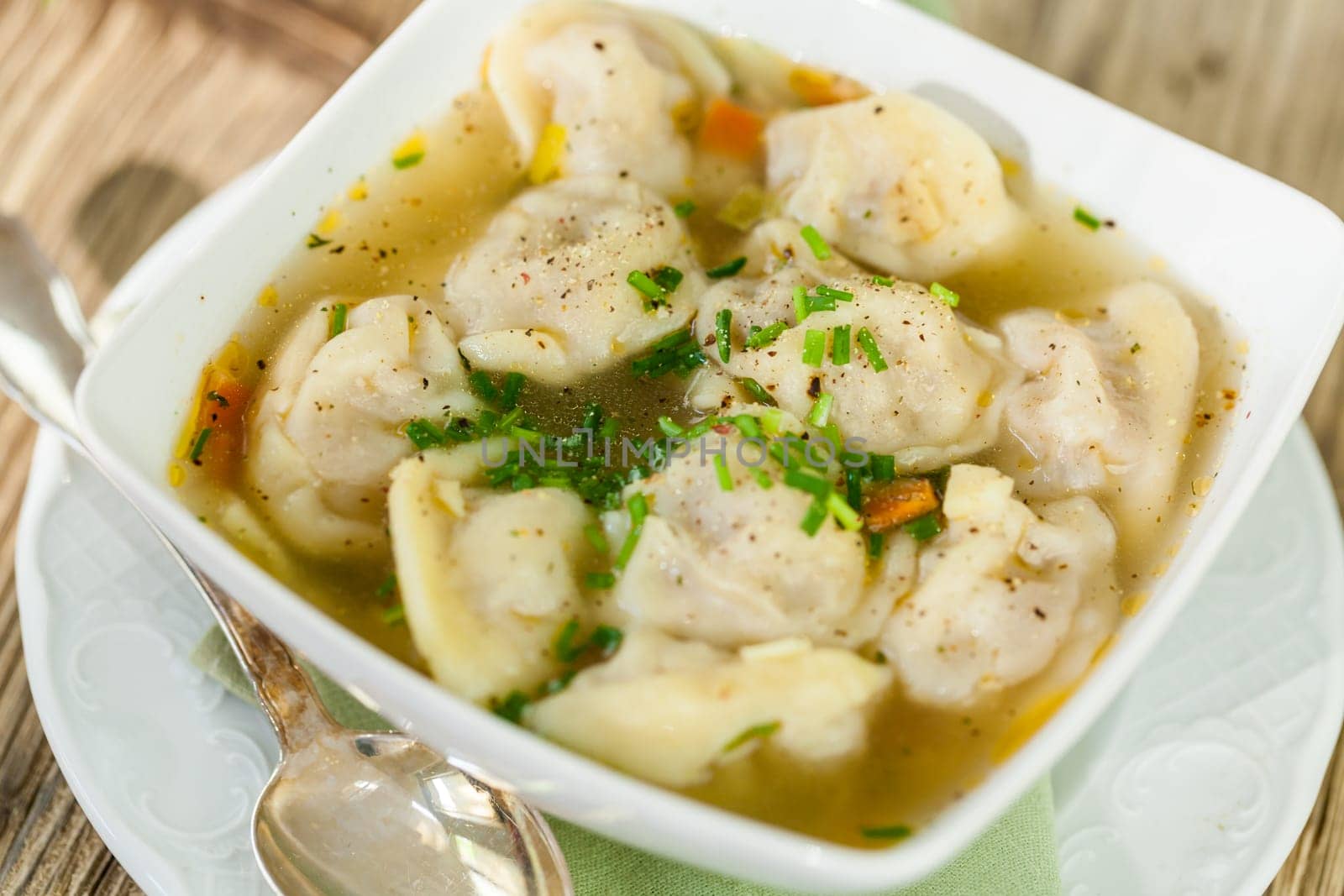 Bowl with Russian Pelmeni Italian tortellini with broth and parsley close-up on a wooden table