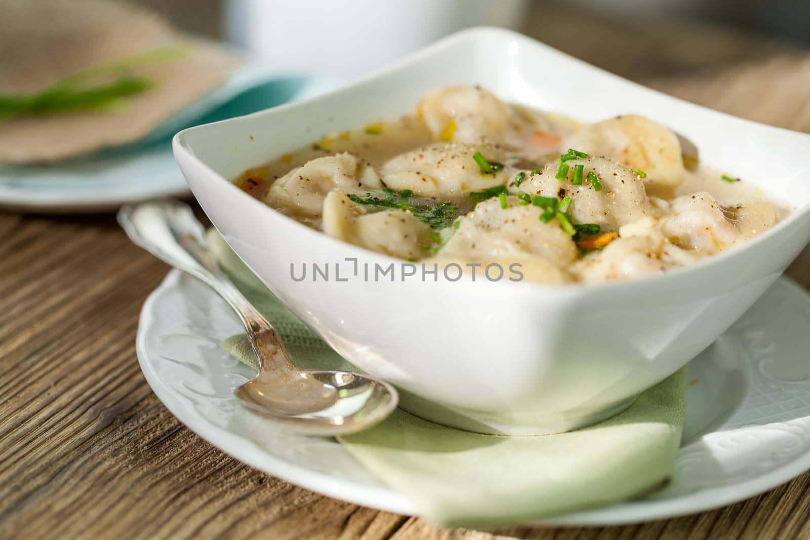 Bowl with Russian Pelmeni Italian tortellini with broth and parsley close-up on a wooden table