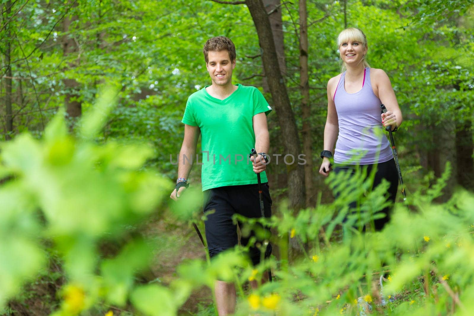 Young spoty active cople with hiking sticks walking in nature. Active lifestyle. Activities and recreation outdoors.