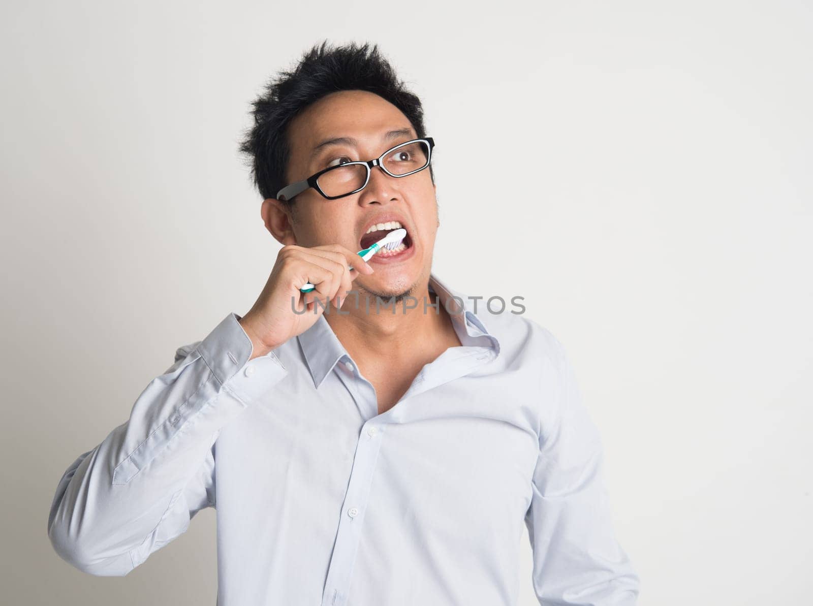 Asian business man woke up late, brushing teeth in hurry, on plain background