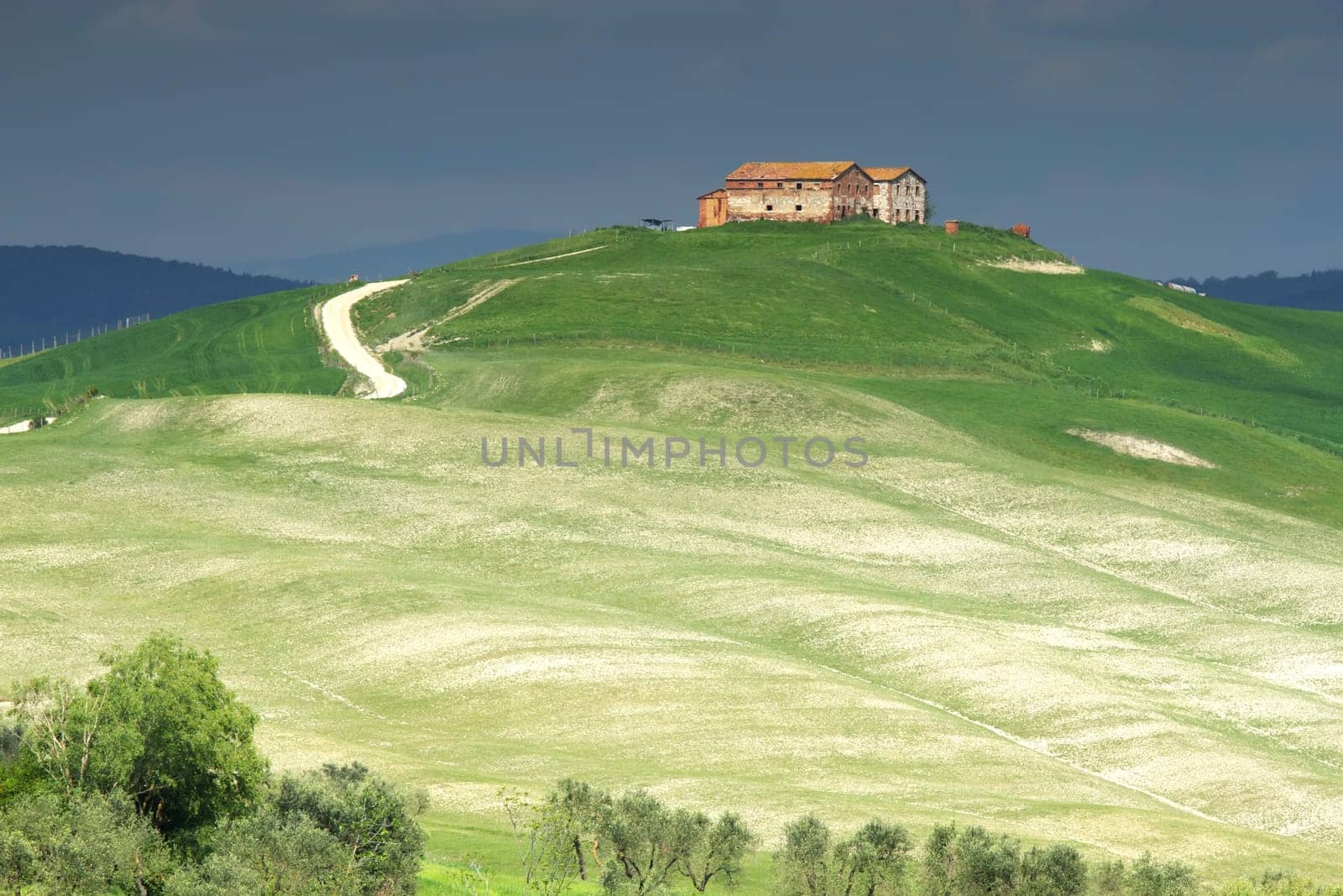 Tuscan  landscape with farmhouse  on the hill. Storm dark sky in the background. .