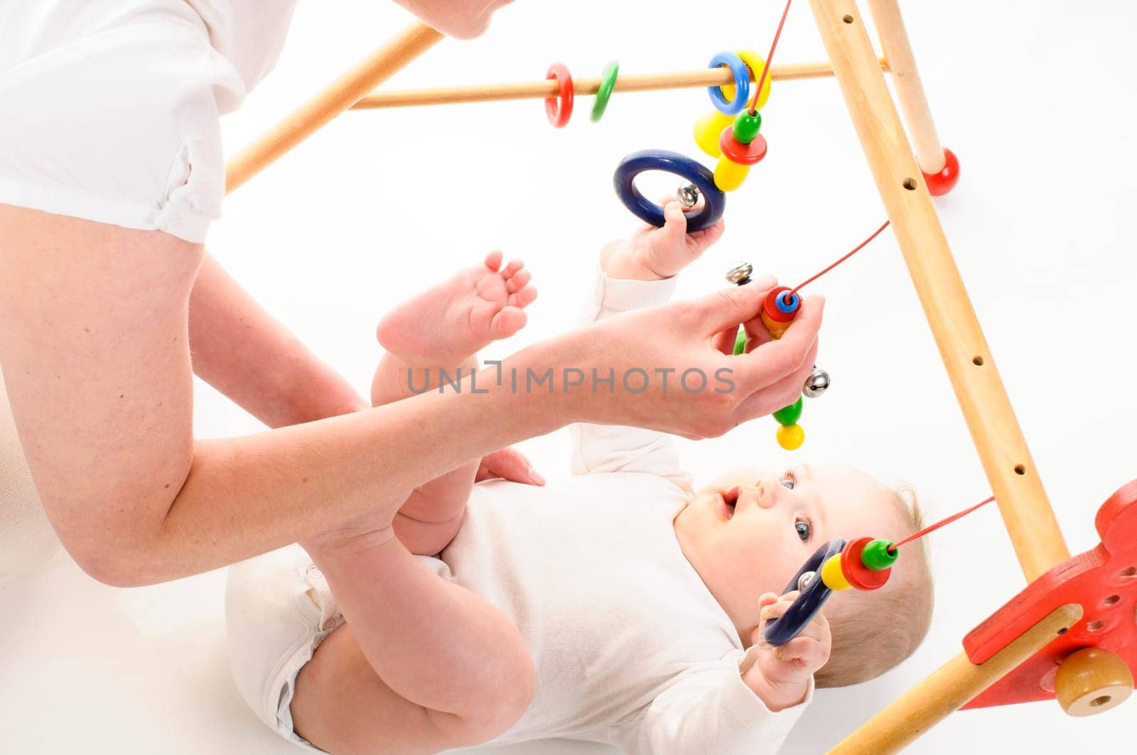 Mother and 6-month-old daughter play together on the floor with wooden toys and play bows,isolated against a white background.