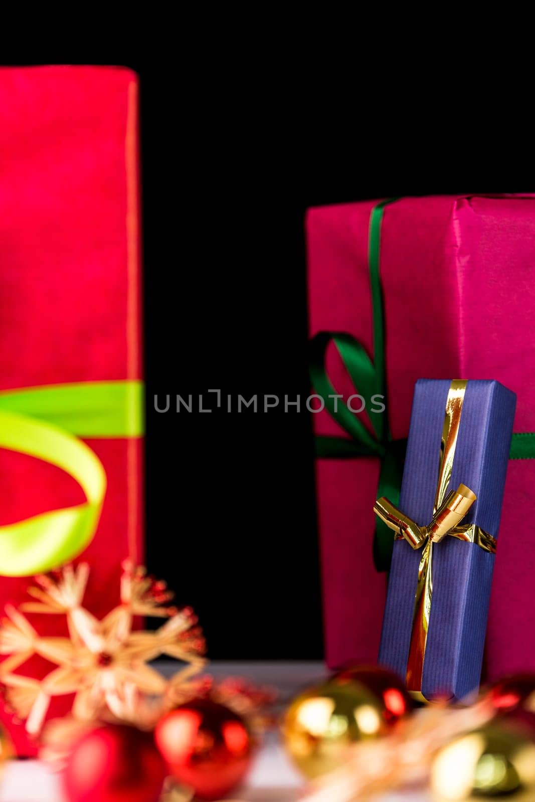 The soft shapes of baubles, straw stars and a crimson gift box are accentuating the sharp outlines of the blue present tied with a golden ribbon in the mid-ground..