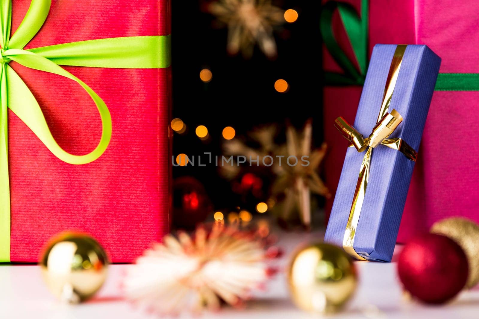 Sharp outlines of a golden bowknot tied around a blue present accentuating the soft forms of glitters, stars and baubles outside the depth of field..