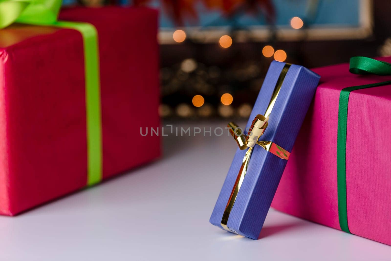Three presents wrapped in blue, red and magenta. Focus is on the golden bowknot, which complements the twinkles in the background..