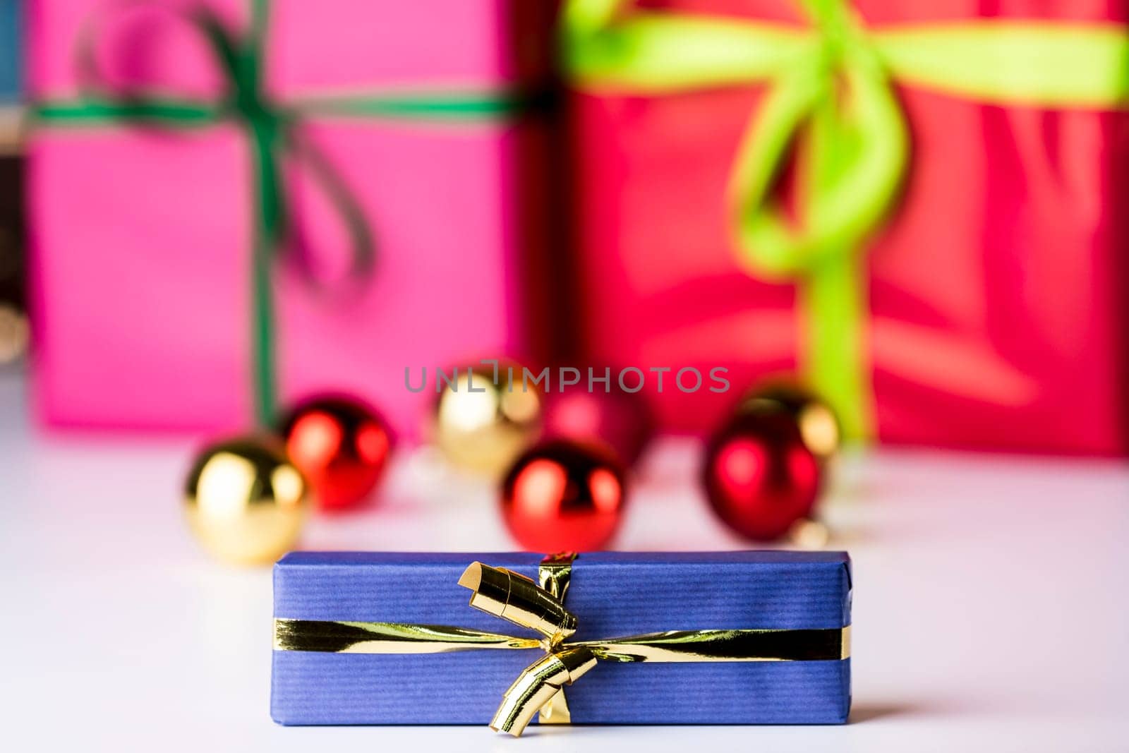 Glitter balls and bowknots in soft focus bring out the sharp contours of the blue wrapped present with the golden bow in the front..