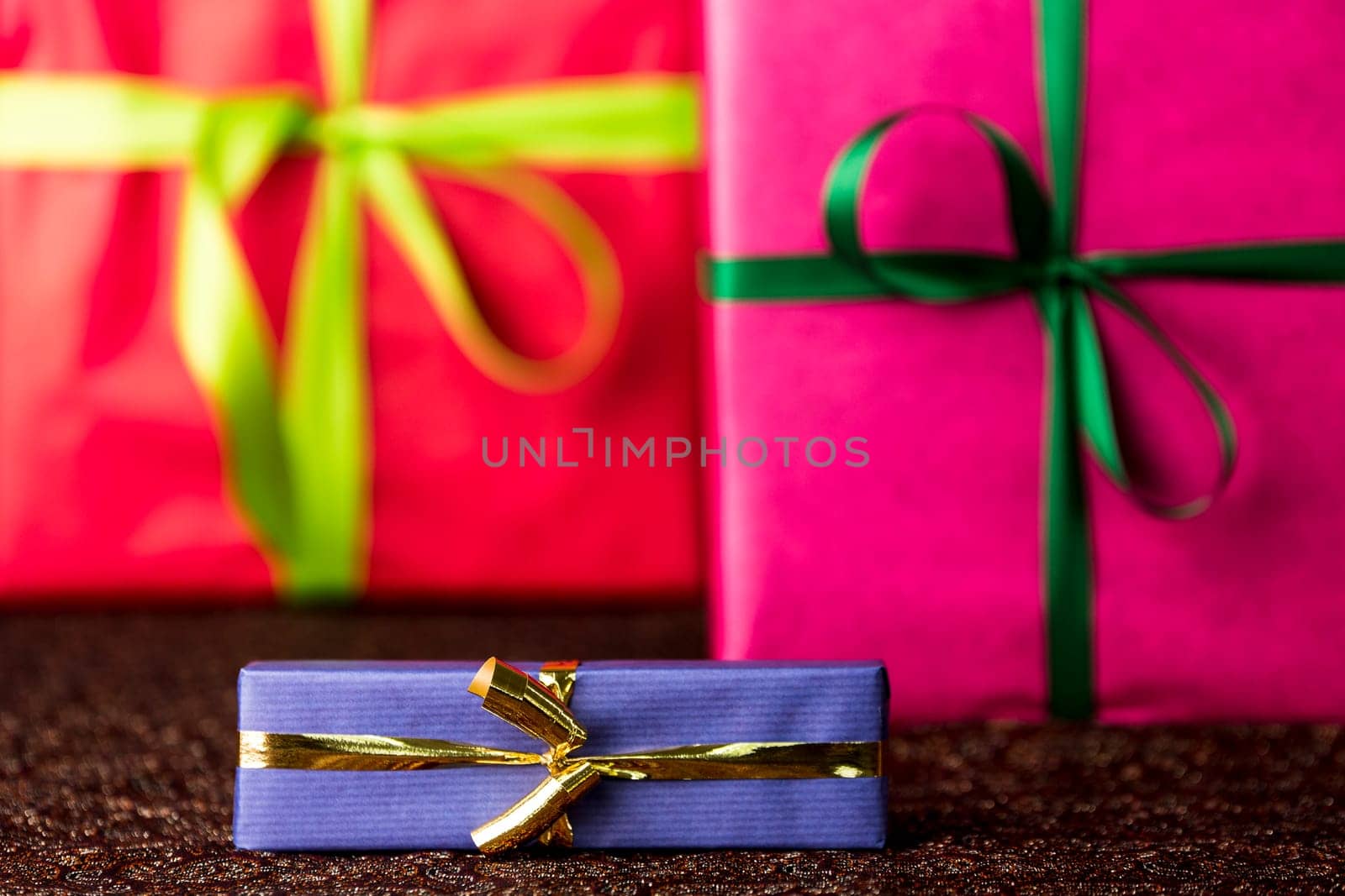 The golden bow and blue wrapping of a small gift box are in focus and do contrast with the red and magenta color-fields of two larger presents..