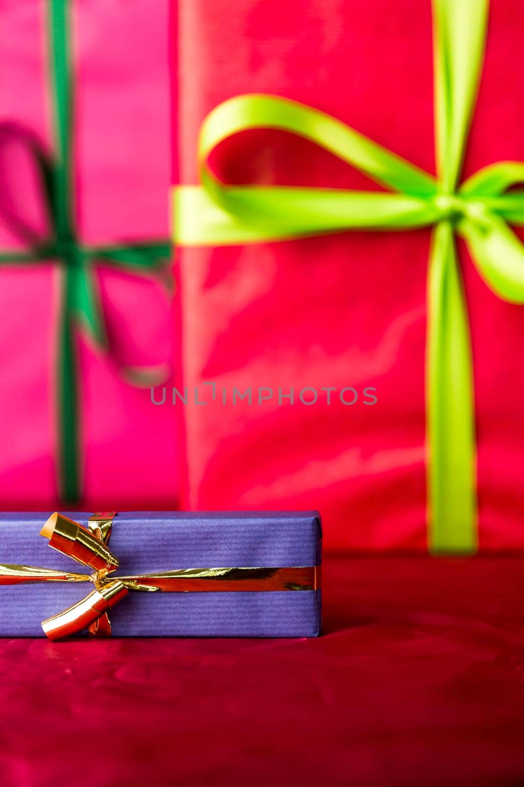 The sharp contours of a blue present tied with a golden ribbon placed against the backdrop of purple cloth and two gifts wrapped in magenta and red..