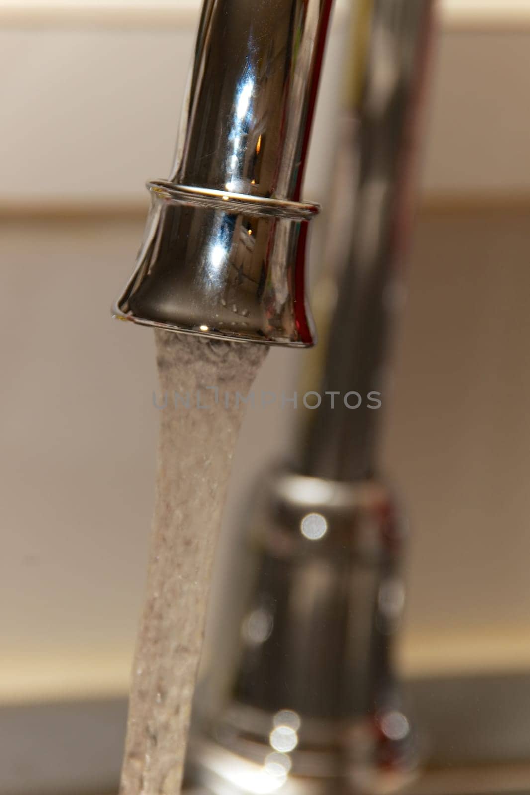 A chrome kitchen water faucet up close with water running.
