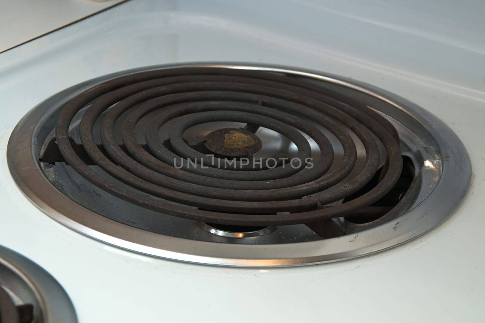 A coiled electric heating element on a modern stove, rusted with chrome ring on white stove top.