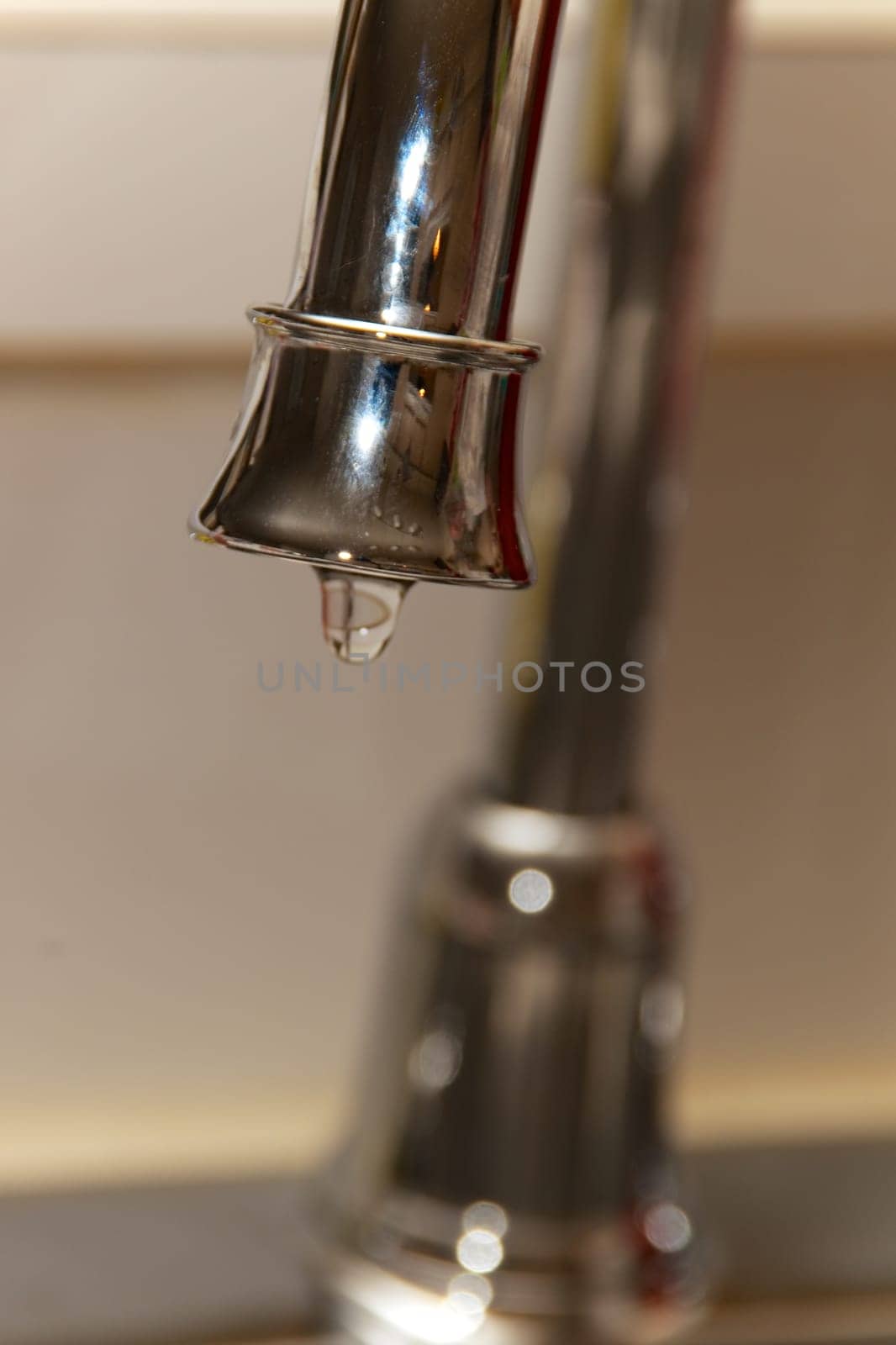 A chrome kitchen water faucet up close with water drop drip.