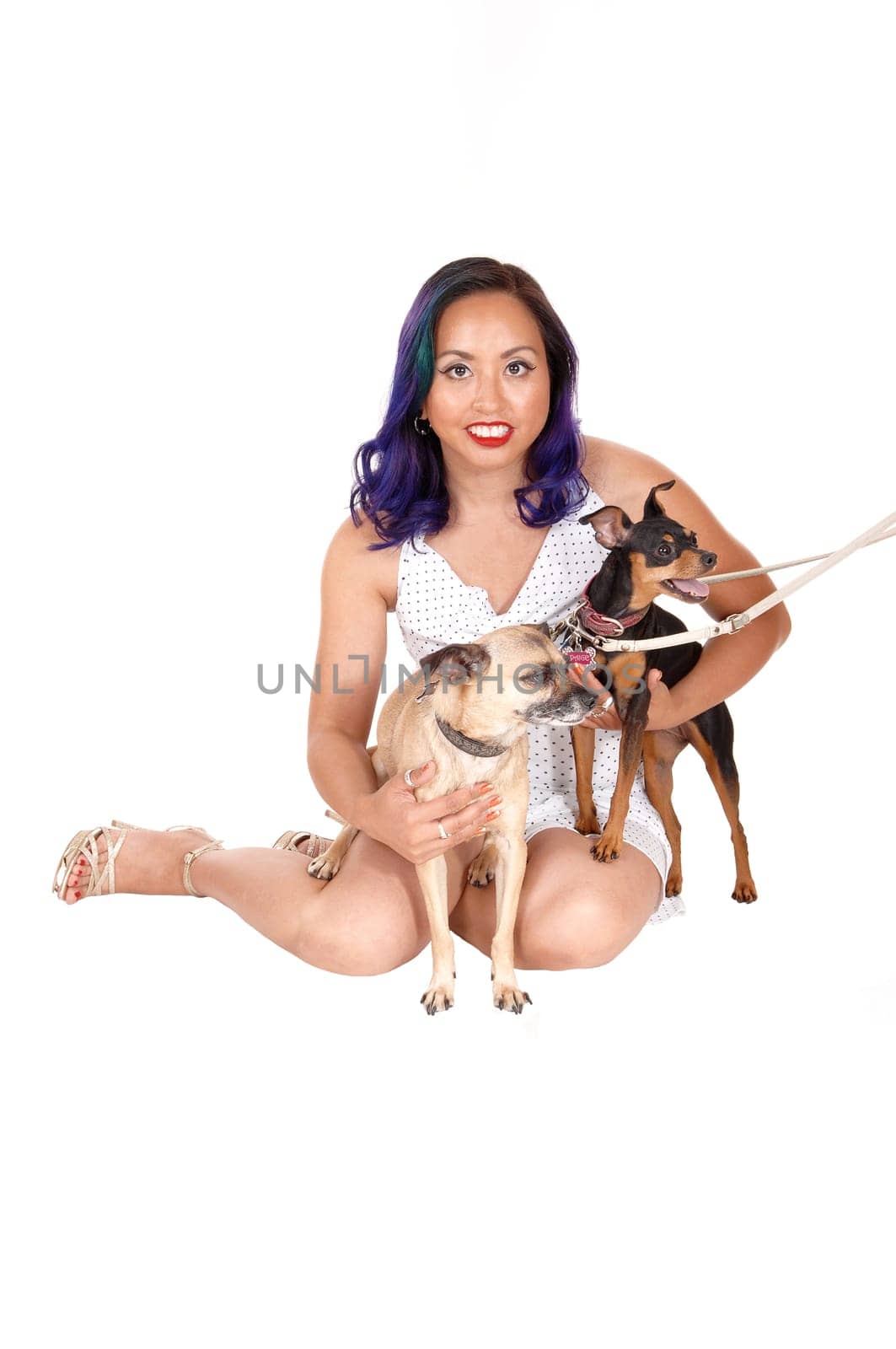 A pretty Asian women sitting on the floor holding her two little dog's.in her arms, isolated over white background..