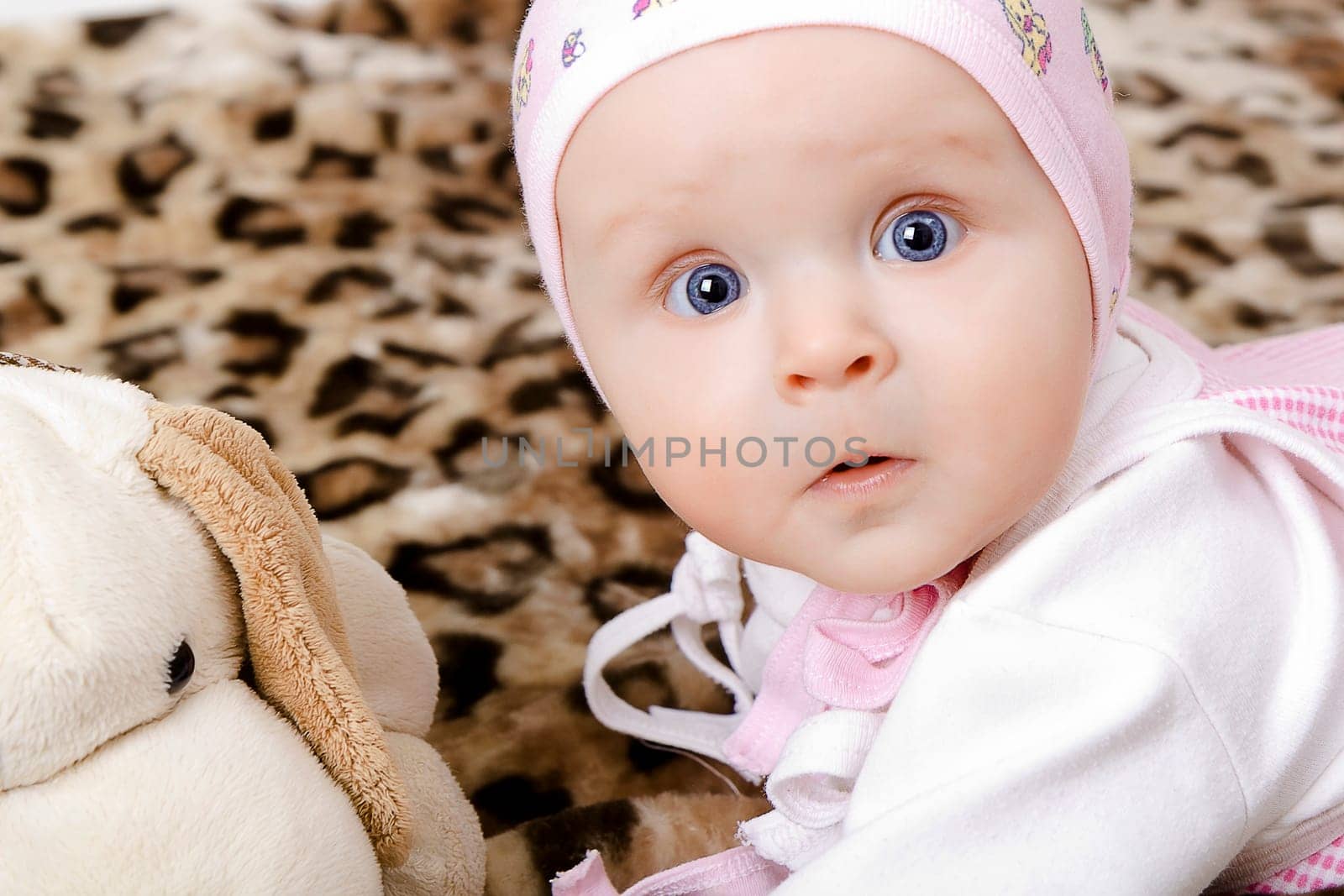 Blue-eyed surprised baby in a cap with a soft toy