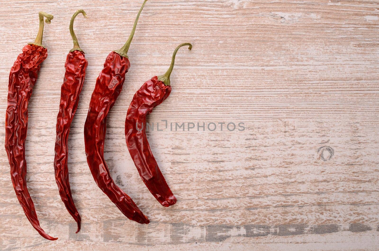 Four dried chilies on a rustic wooden background with space for text