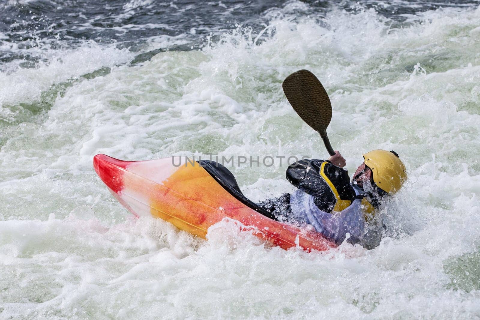 an active male kayaker rolling and surfing in rough water