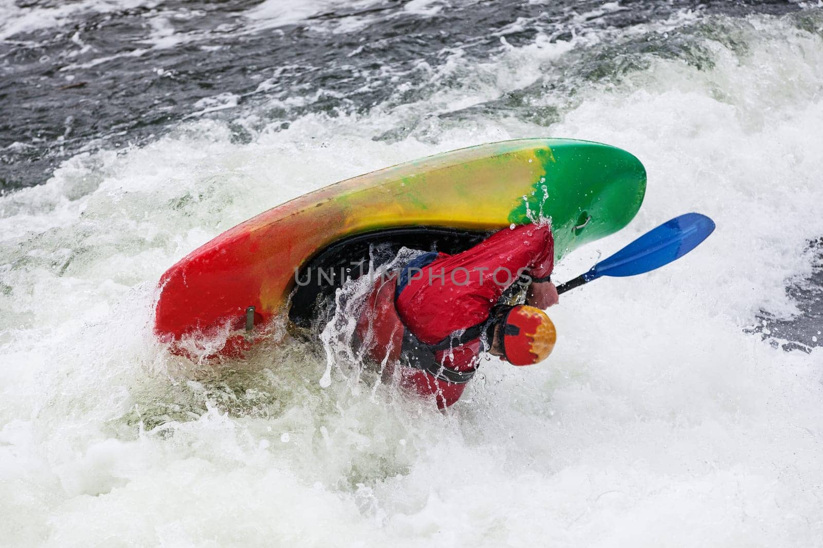 an active male kayaker rolling and surfing in rough water