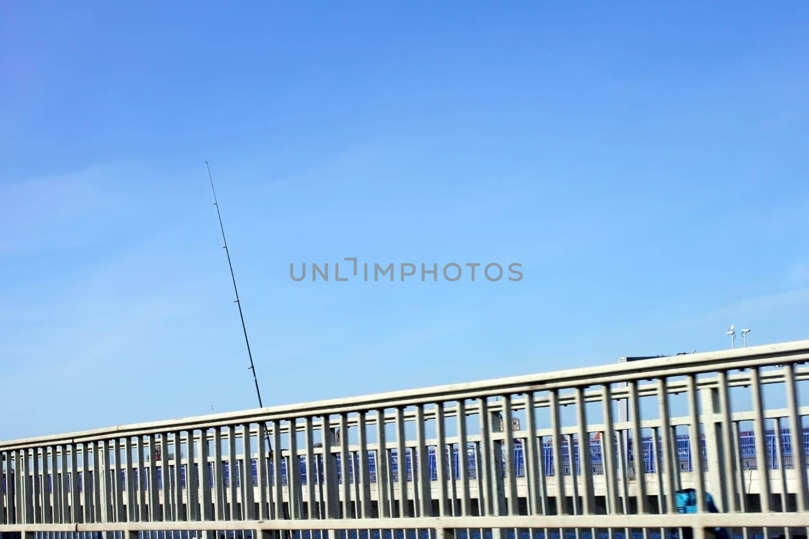 The photograph of a bridge railing with a leaning fishing rod.