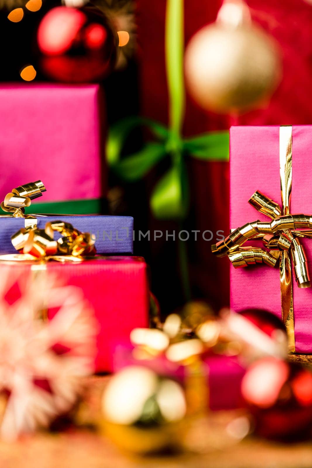 Christmas presents in solid colors between baubles and straw stars. Focus is on the golden bow knot around the magenta box. Seasonal background with shallow depth of field..