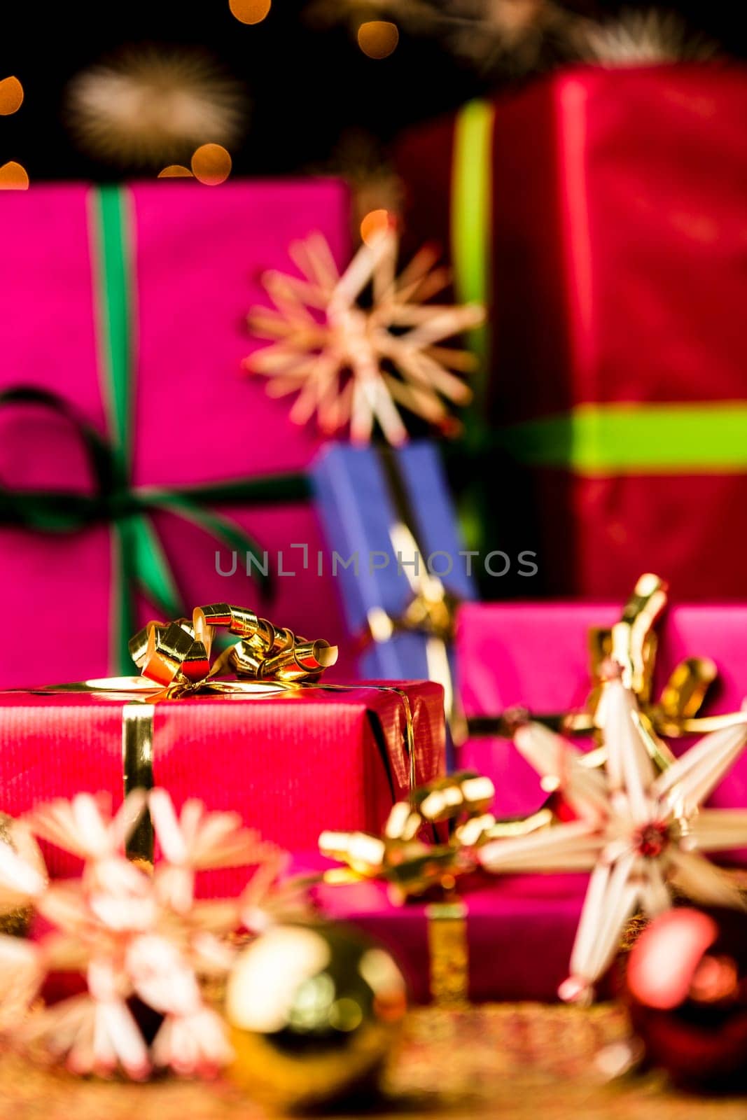 Six Christmas presents in monochrome gift-wrapping. Focus is set on the golden bow around the small crimson red gift on the left. Baubles and stars are outside the shallow depth of field..
