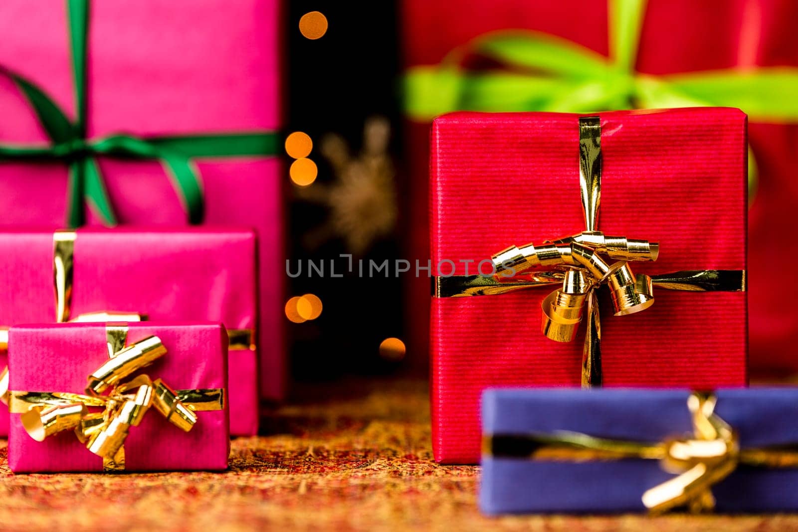 Christmas presents in plain colors placed on a festive cloth. Seasonal background with plenty of text space. Shallow depth of field. Crimson box in focus..