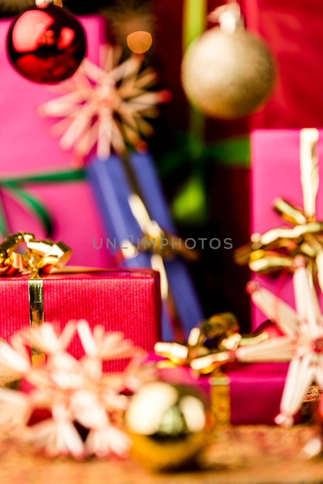 Christmas gifts in vibrant colors between stars and baubles. Focus is on the front plane of the small crimson packet with the golden bow. Atmospheric background with shallow depth of field..