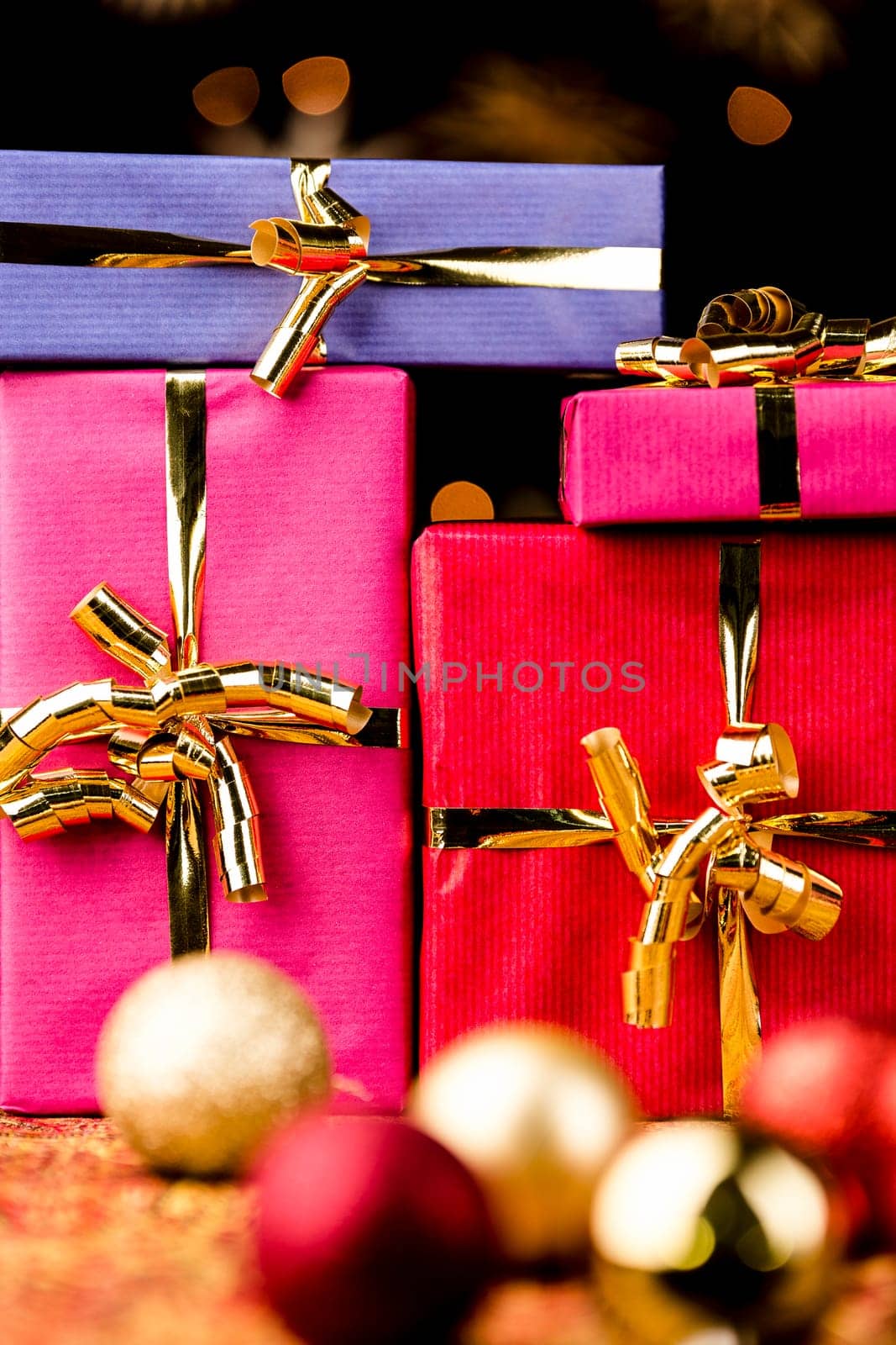 Close-up shot of presents wrapped with golden bows. Tightly framed. Shallow depth of field. Blurred baubles in the front. Background for Christmas and other festive occasions..