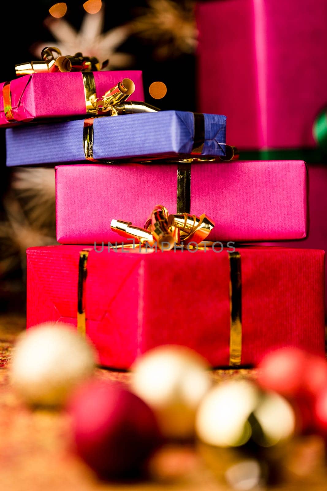 Four Christmas gift boxes with golden bows piled up. Tight framing,vibrant colors. Blurred baubles in the foreground. Background for Xmas gift-giving..