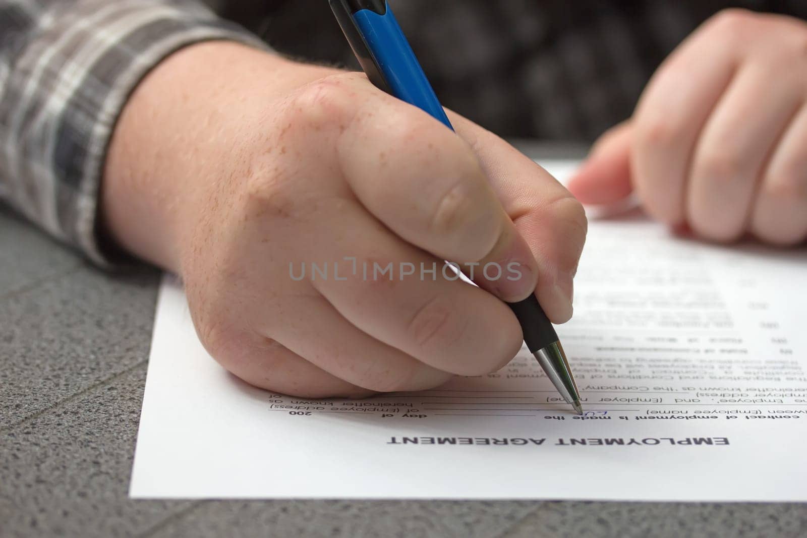 Closeup view of a hand of worker filling the form of employment agreement outdoors.