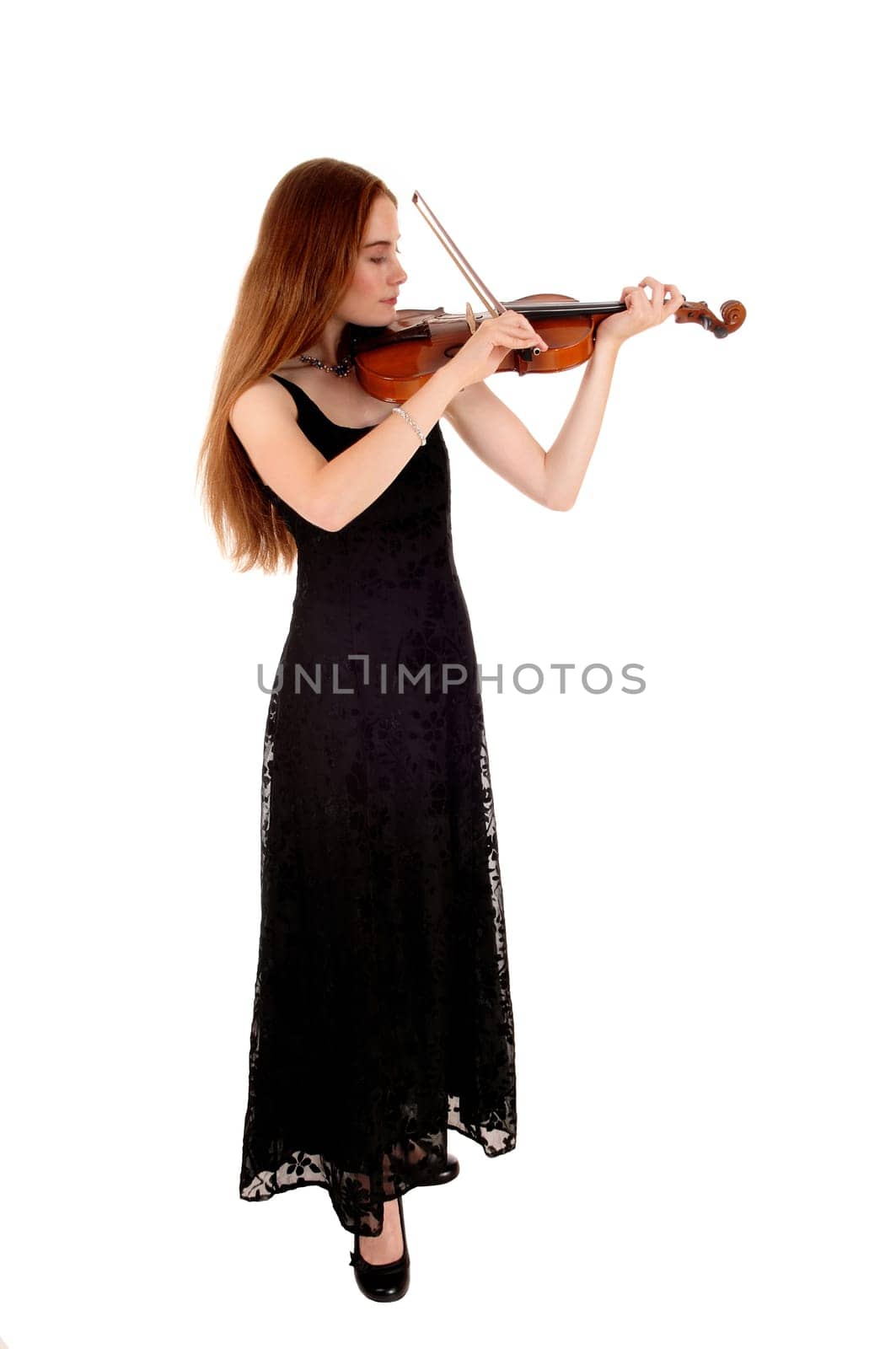 A slim young woman in a long black dress standing for white background.playing the violin..