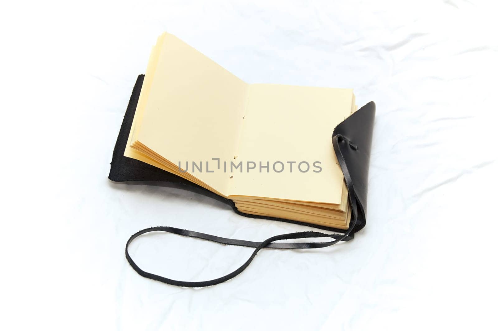 An old fashioned leather bound blank journal open to blank pages shot on white fabric.