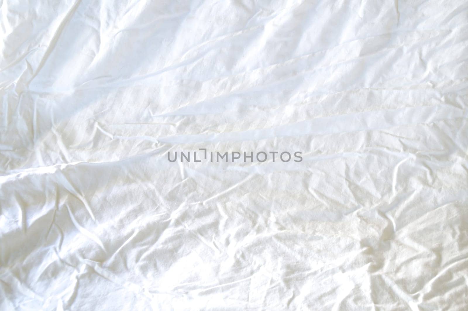 A large white rumpled and wrinkled sheet fills the frame lit with morning light.