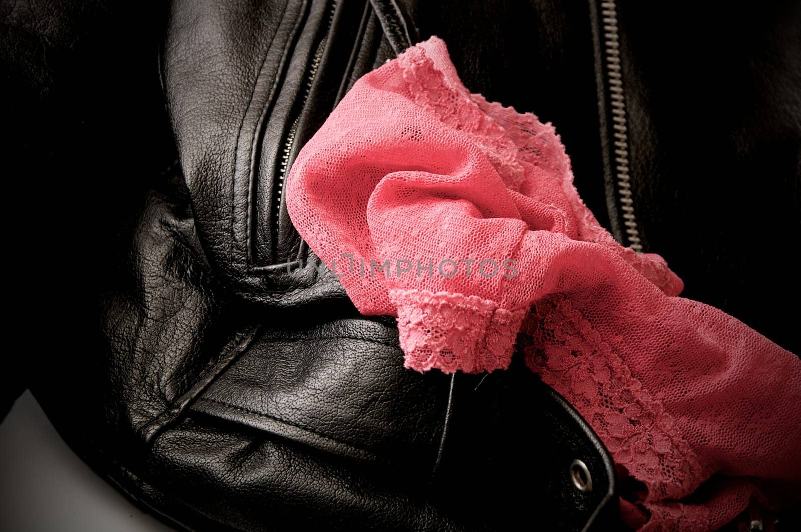 A pair of woman's pink lace panties is draped upon a man's black leather jacket.