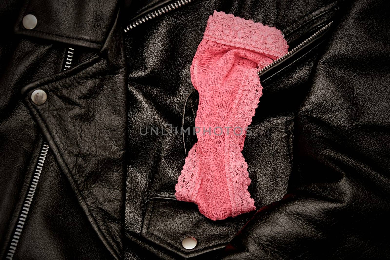 A pair of woman's pink lace panties is draped upon a man's black leather jacket.