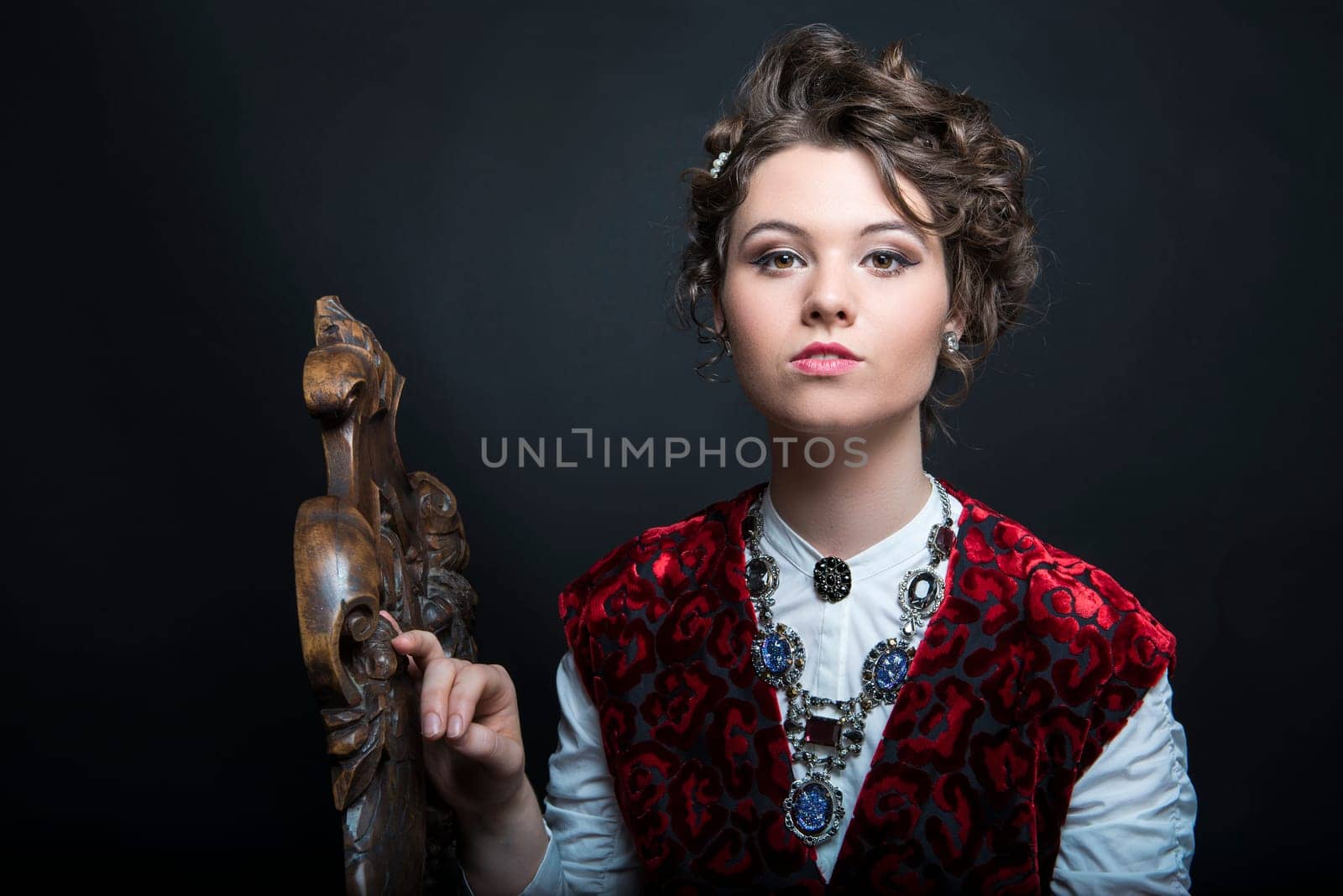 Portrait of beautiful Caucasian model in red Victorian-style velvet dress, seated on wooden chair