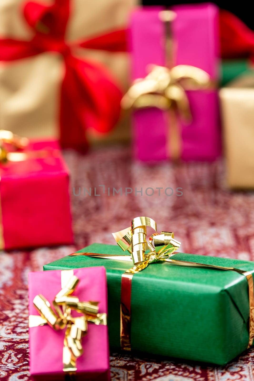 Green gift box between other plain-colored presents wrapped in magenta, gold and red. Tight close-up shot with shallow depth of field.